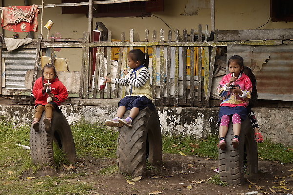 three little schoolgirls sitting on three heavy truck tires